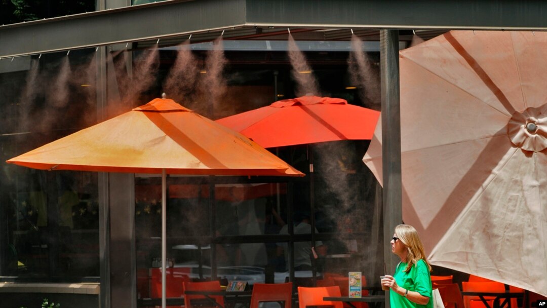 A woman walks under misters outside a restaurant, July 12, 2023 in Gilbert, Ariz. Even desert residents accustomed to scorching summers are feeling the grip of an extreme heat wave smacking the U.S. Southwest this week.