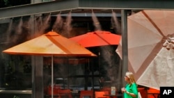 A woman walks under misters outside a restaurant, July 12, 2023 in Gilbert, Ariz. Even desert residents accustomed to scorching summers are feeling the grip of an extreme heat wave smacking the U.S. Southwest this week.