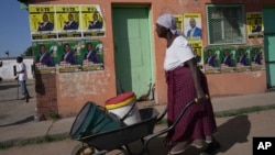 FILE - An elderly woman pushes a wheelbarrow past campaign posters in Mabvuku on the outskirts of Harare, Zimbabwe, Dec. 9, 2023. 