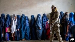 FILE - A Taliban fighter stands guard as women wait to receive food rations distributed by a humanitarian aid group, in Kabul, Afghanistan, May 23, 2023. 