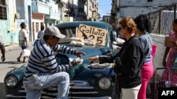 Seorang pria menjual kue di mobil tua Amerika di Havana, 20 Desember 2023. (YAMIL LAGE/AFP)