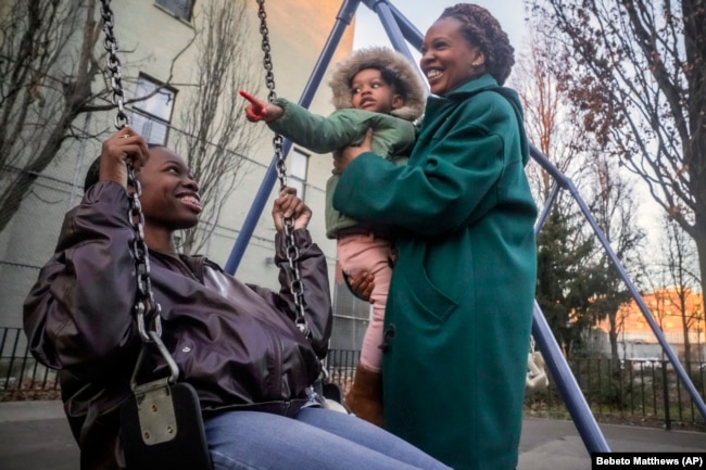 Derry Oliver, right, holds daughter Dessie, 2, while her other daughter, also named Derry, swings, Feb. 9, 2024, in New York. (AP Photo/Bebeto Matthews)