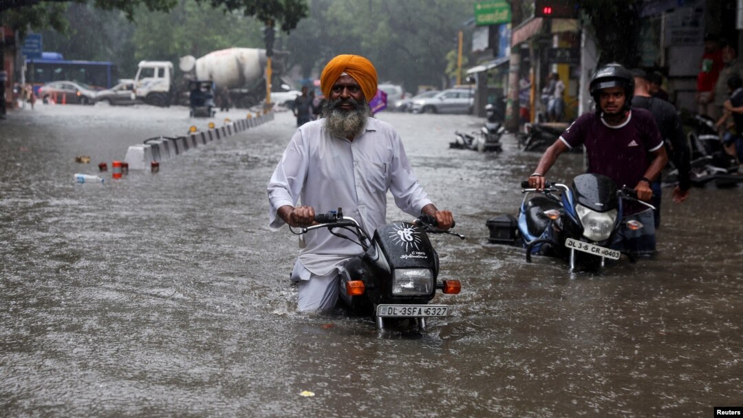 Dua pria mengendarai sepeda motornya mengarungi jalanan yang terendam banjir setelah hujan lebat di New Delhi, India (8/7). 