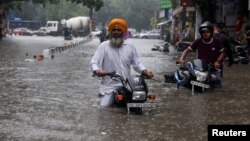 Dua pria mengendarai sepeda motornya mengarungi jalanan yang terendam banjir setelah hujan lebat di New Delhi, India (8/7). 