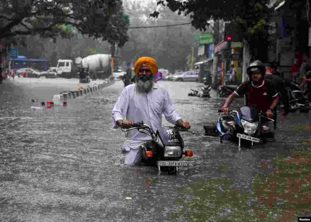 Men wade through a flooded street with their motorbikes after heavy rains in New Delhi, India.