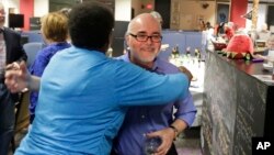 FILE - Charlotte Observer editorial cartoonist Kevin Siers, right, gets a hug from a co-worker as they celebrate Siers winning the Pulitzer Prize for Editorial Cartooning at the newspaper in Charlotte, North Carolina, April 14, 2014. Siers was among cartoonists laid off last week