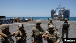U.S. soldiers stand at Trident Pier, a temporary pier to deliver aid, off the Gaza Strip, amid the ongoing conflict between Israel and Hamas, near the Gaza coast, June 25, 2024, as an aid truck drives off a ship in the background.