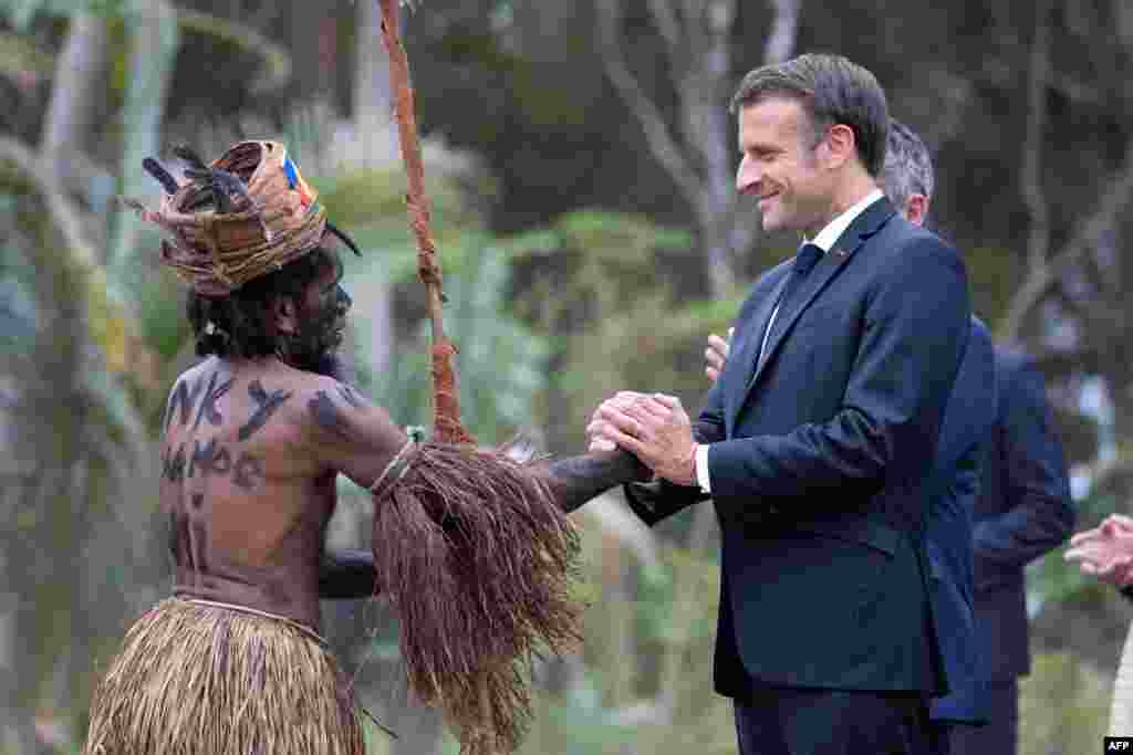Францускиот претседател Емануел Макрон се ракува со традиционален танчер за време на вообичаената церемонија во негова чест во Тухо, северно од Нова Каледонија.