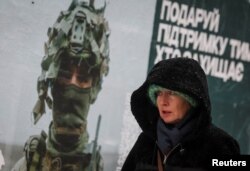 Žena prolazi pored plakata ukrajinskog vojnika dok pada snijeg u Kijevu.