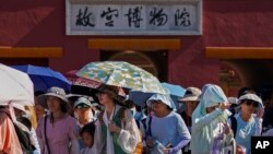 Pengunjung mengenakan topi dan membawa payung saat meninggalkan Kota Terlarang (Forbidden City) di Beijing, pada hari yang panas, Kamis, 29 Juni 2023. (AP/Andy Wong)