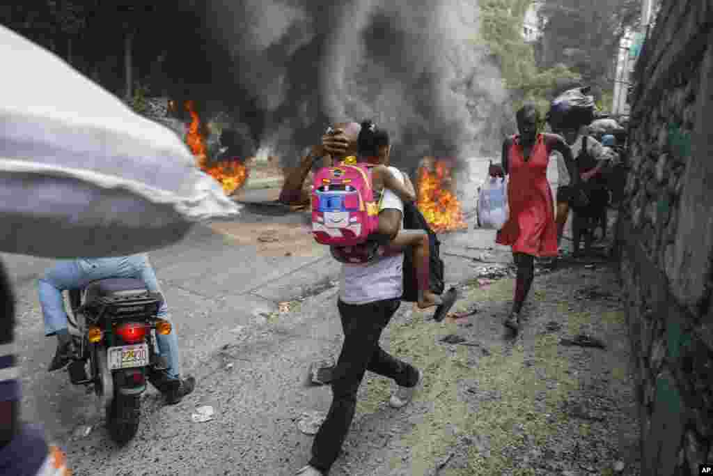 Луѓето поминуваат покрај запалените гуми за време на протестот против премиерот на Хаити Ариел Хенри во Порт-о-Пренс, 5 февруари 2024 година. Банките, училиштата и владините агенции се затворени во северните и јужните региони на Хаити, бидејќи, според известувањето на локалните медиуми, демонстрантите ги блокираа главните патишта со запалени гуми и парализираа јавен превоз.