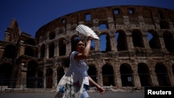 Seorang turis tampak melindungi wajahnya dari sinar matahari dengan kipas yang ia bawa saat berkunjung ke Colosseum di tengah gelombang panas yang menyerang Roma, pada 11 Juli 2023. (Foto: Reuters/Guglielmo Mangiapne)