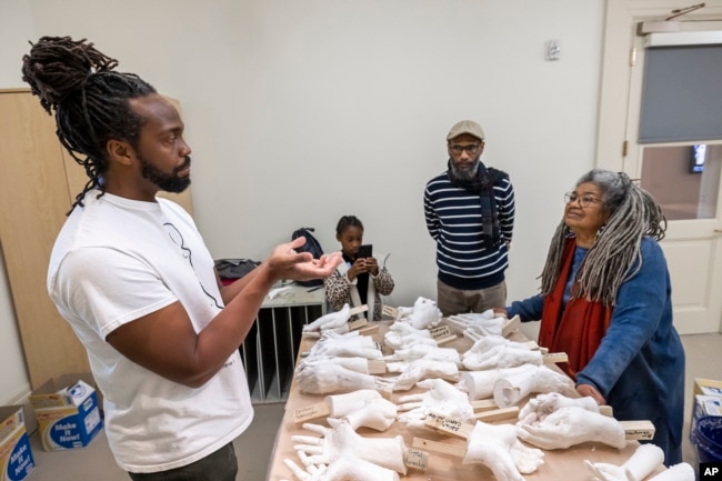 Artist Stephen Hayes, at left, shows volunteers Jonathan Richardson and Arianne King-Comer how to properly hold their hands in a mold in Charleston, S.C., Saturday, Feb. 18, 2023. (AP Photo/Mic Smith)