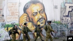 FILE - Israeli soldiers patrol at Kalandia checkpoint between Jerusalem and the West Bank city of Ramallah, March 8, 2012, in front of a mural of jailed Fatah leader Marwan Barghouti.