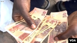 A Zimbabwean holds local currency in Harare on Feb. 13, 2024. Known as the dollar, bondnotes or ZWL, the currency has become nearly worthless since its introduction in 2014. (Columbus Mavhunga/VOA)