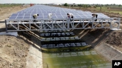 FILE - Workers give finishing touches to installed solar panels covering the Narmada canal ahead of its inauguration at Chandrasan village, near Ahmadabad, India, April 22, 2012. It was the first project of its kind in the world.