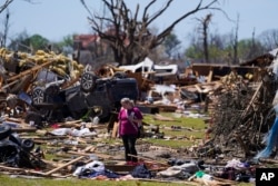 A woman walks near an uprooted tree, a flipped vehicle and debris from homes damaged by a tornado, March 27, 2023, in Rolling Fork, Miss. (AP Photo/Julio Cortez, File)