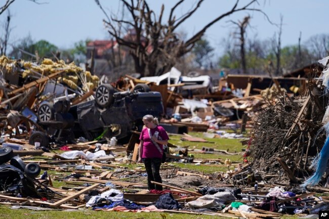 A woman walks near an uprooted tree, a flipped vehicle and debris from homes damaged by a tornado, March 27, 2023, in Rolling Fork, Miss. (AP Photo/Julio Cortez, File)