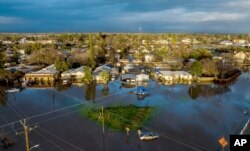 FILE - Following days of rain, floodwaters surround homes and vehicles in the Planada community of Merced County, California, Jan. 10, 2023.