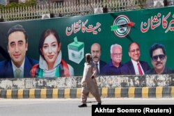 Seorang pria berjalan di samping papan reklame yang memajang foto politisi Bilawal Bhutto dan saudara perempuannya Asifa Bhutto, sehari setelah pemilihan umum di Karachi, Pakistan, 9 Februari 2024. (Foto: REUTERS/Akhtar Soomro)