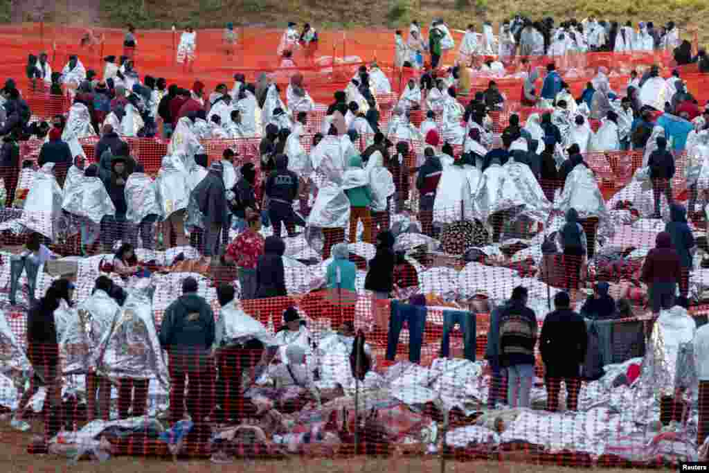 Migrants wear mylar blankets supplied by the U.S. Border Patrol to keep warm in the early hours of the morning after spending the night in an outdoor processing center in Eagle Pass, Texas, Dec. 20, 2023. 