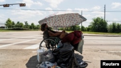 Tony, a homeless man, sits under his umbrella to avoid sun light during hot weather in Houston, Texas, June 28, 2023. 