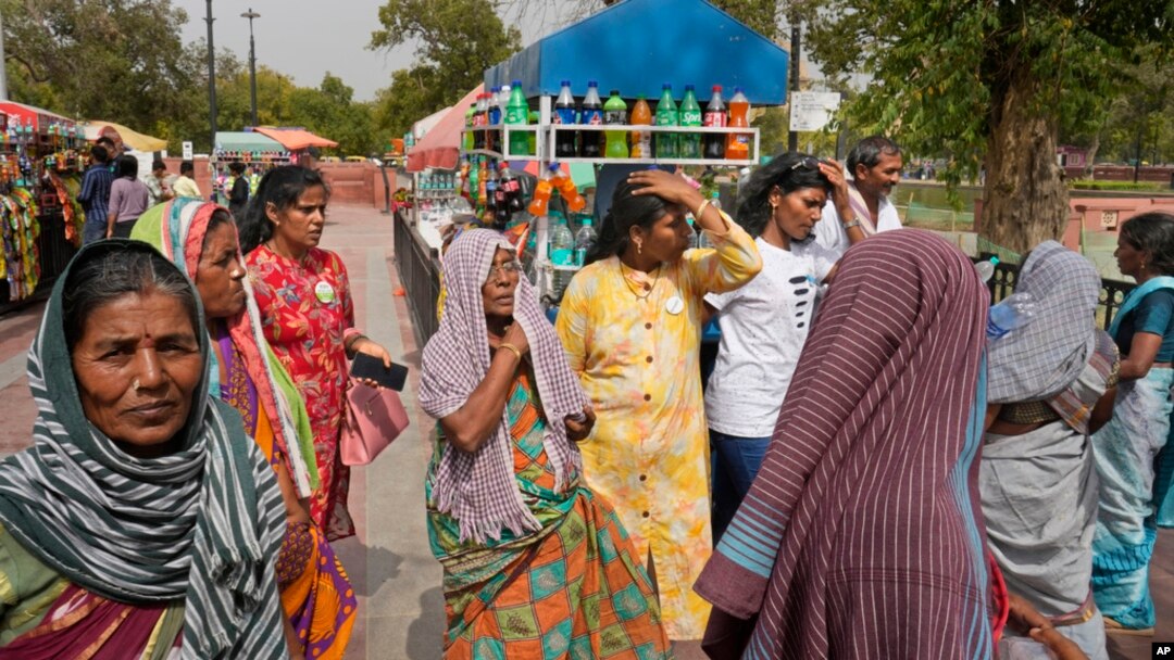People cover their heads to shield from the heat as they buy water bottles in New Delhi, India, Tuesday, June 18, 2024.