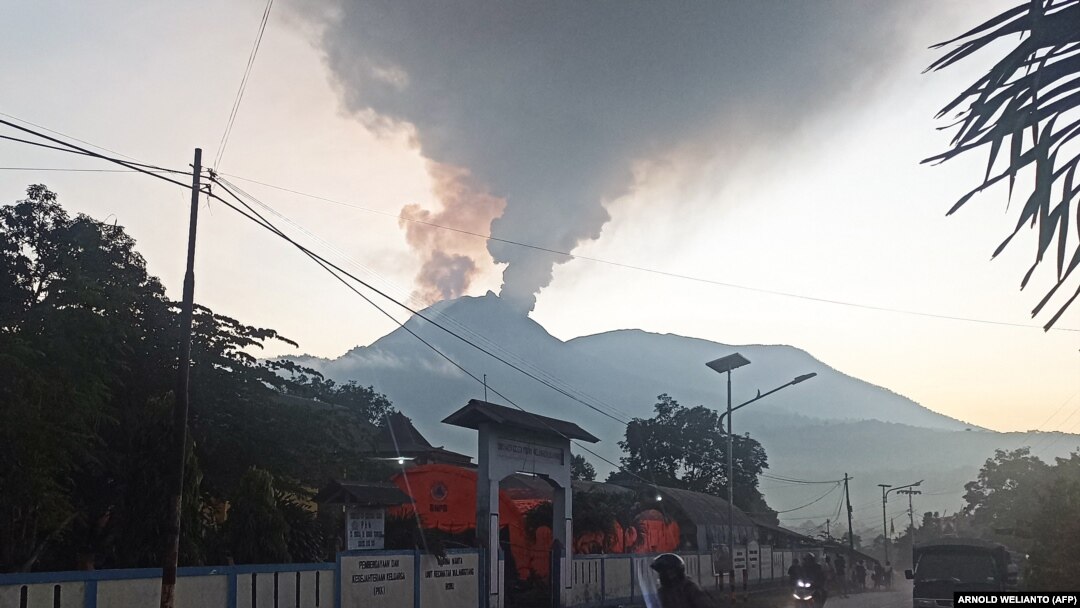 Pengendara berkendara saat Gunung Lewotobi Laki-Laki mengeluarkan asap panas di Flores Timur, Nusa Tenggara, Timur, 2 Januari 2024. (Foto: AFP/ARNOLD WELIANTO)