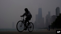 FILE - A person rides a bicycle along the shore of Lake Michigan as Chicago's downtown skyline is blanketed in haze from Canadian wildfires, in Chicago, Illinois, June 27, 2023.