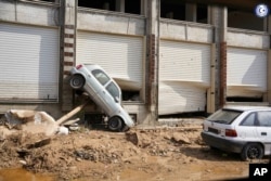 In this photo provided by the Libyan government, a car sits suspended against a shop front after being carried by floodwaters in Derna, Libya, on Monday, Sept. 11, 2023. (Libyan government via AP)