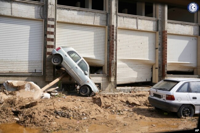 In this photo provided by the Libyan government, a car sits suspended against a shop front after being carried by floodwaters in Derna, Libya, on Monday, Sept. 11, 2023. (Libyan government via AP)
