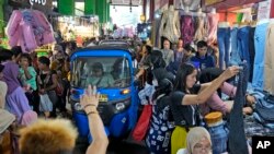 Sebuah "bajaj" melewati kerumunan pembeli pada minggu terakhir Ramadan, di pasar Tanah Abang , Jakarta, Jumat, 14 April 2023. (AP/Dita Alangkara)