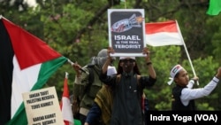 Sejumlah peserta aksi bela Palestina mengibarkan bendera Indonesia, bendera Palestina dan poster bertuliskan "Israel adalah Teroris yang Sebenarnya," di lapangan Monas, Minggu, 5 November 2023. (Foto: Indra Yoga/VOA)