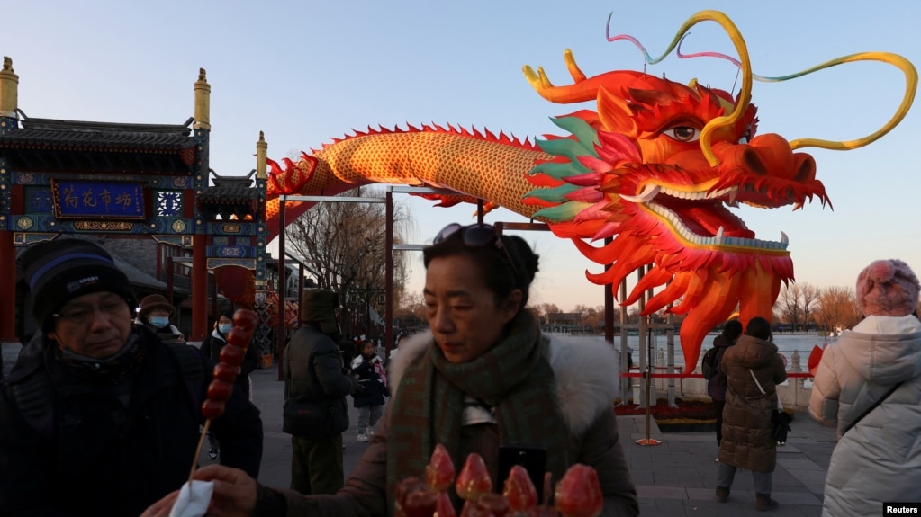 北京一个公园里庆祝龙年的装饰前一名女子在买糖葫芦。(2024年2月7日)