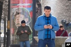 Muškarci gledaju u svoje telefone dok prolaze pored bilborda za regrutaciju vojske sa natpisom "Vojna služba po ugovoru u oružanim snagama" u Sankt Peterburgu, Rusija, 12. aprila 2023.