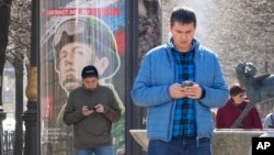 Men look at their phones walking past an army recruiting billboard with the words 'Military service under contract in the armed forces,' in St. Petersburg, Russia, April 12, 2023.