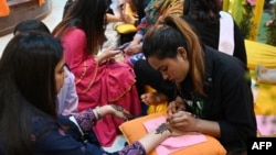Beauticians apply henna designs on a customer's hand at a mall ahead of Eid al-Fitr festival, which marks the end of the holy fasting month of Ramadan, in Islamabad on April 21, 2023.