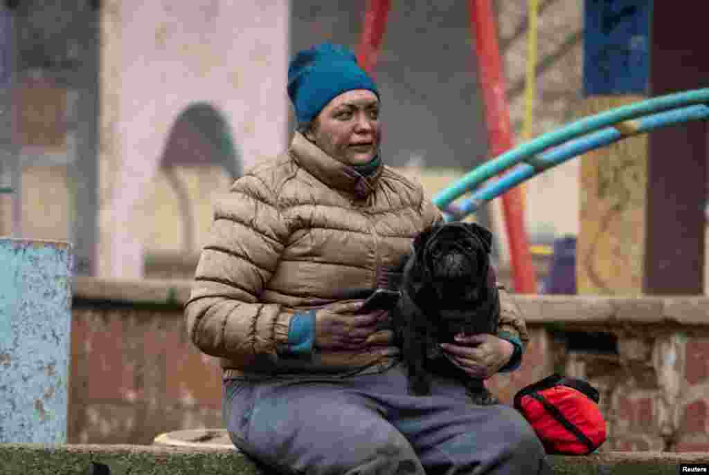 A local resident with her dog sits near her residential building damaged during a Russian missile strike in Kyiv, Ukraine.