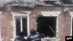 FILE - Petugas penegak hukum berdiri di samping sebuah rumah yang rusak akibat serangan rudal di Zolochiv, wilayah Kharkiv, 6 Februari 2024. (Handout / KANTOR KEJAKSAAN JENDERAL UKRAINA/AFP)