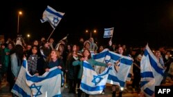 Сторонники держат флаги, когда израильские заложники прибывают в автомобиле на военную базу Офаким на юге Израиля рано утром 30 ноября 2023 года