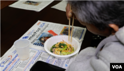 Phal Sann, 61, eats soup and reads the Khmer Post USA at the income tax office of Rithy Sao in Lowell, Massachusetts. (Sisovann Pin/VOA)