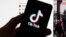 FILE - The TikTok logo is seen on a mobile phone in front of a computer screen which displays the TikTok home screen, March 18, 2023, in Boston. 