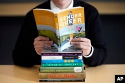 FILE - Amanda Darrow, director of youth, family and education programs at the Utah Pride Center, poses with books that have been the subject of complaints from parents on Dec. 16, 2021. (AP Photo/Rick Bowmer, File)