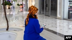 A Turkmen woman wearing a traditional dress reads news on her smartphone in Ashgabat, Turkmenistan, Jan. 31, 2024. 