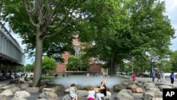 FILE - People relax near a fountain at Harvard University, June 29, 2023, in Cambridge, Mass. 