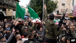 Palestinian gunmen march with bodies of militants, draped in the flags of the Palestinian Islamic Jihad, killed in an Israeli military raid at Ibn Sina Hospital in the West Bank town of Jenin, Jan. 30, 2024.