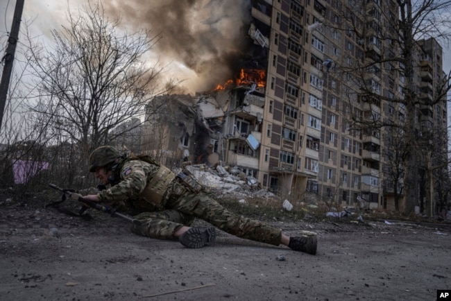 FILE - A Ukrainian police officer takes cover in front of a burning building that was hit in a Russian airstrike in Avdiivka, Ukraine, March 17, 2023.