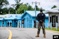 FILE - A South Korean soldier (R) and United Nations Command soldiers (background, in green) stand guard near the military demarcation line separating North and South Korea, at the Joint Security Area of the DMZ, in the truce village of Panmunjom, Oct. 4, 2022.