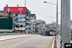 Myanmar nationals walk on the Thailand-Myanmar Friendship Bridge, with a Myanmar flag flying atop the border control building on the Myanmar side (right), as seen from the Mae Sot region of Thailand on April 12, 2024.