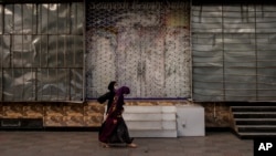 FILE - Women walk past a shuttered beauty salon in Kabul, Afghanistan, Sept. 11, 2021.